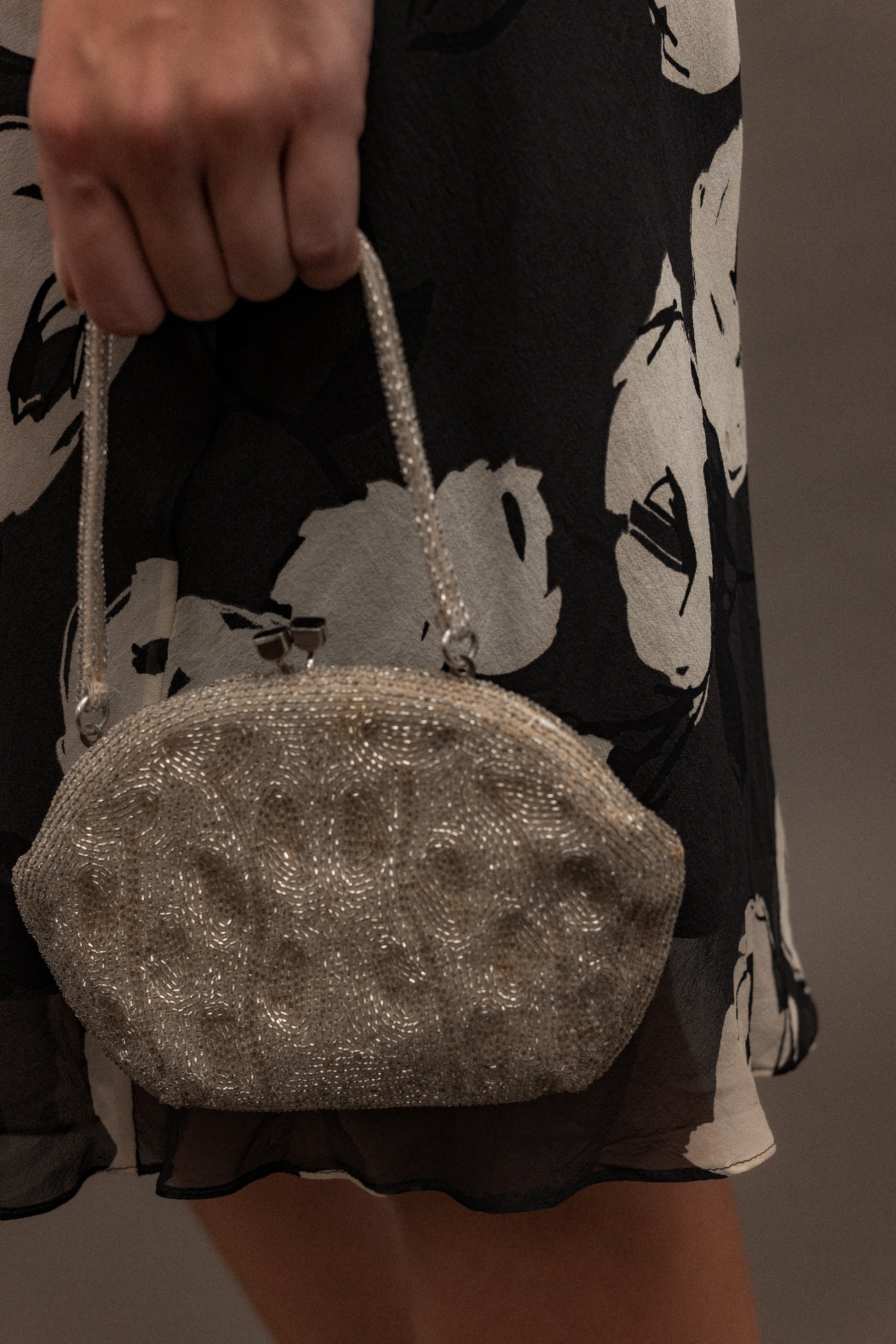 Silver glittery handbag held by a person wearing a black and white patterned dress.